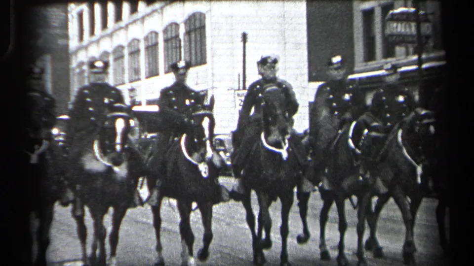Mounted police officers on horseback ride in formation through Cleveland street surroundings in the supplied 1937 home-movie footage.