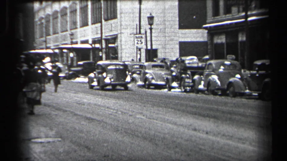 Wide 1937 Cleveland street view with parked vintage automobiles, masonry buildings, a speed sign, and mounted police farther down the road.