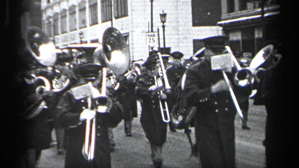 Uniformed brass players with trumpets or similar instruments pass the camera during the 1937 Cleveland parade scene.