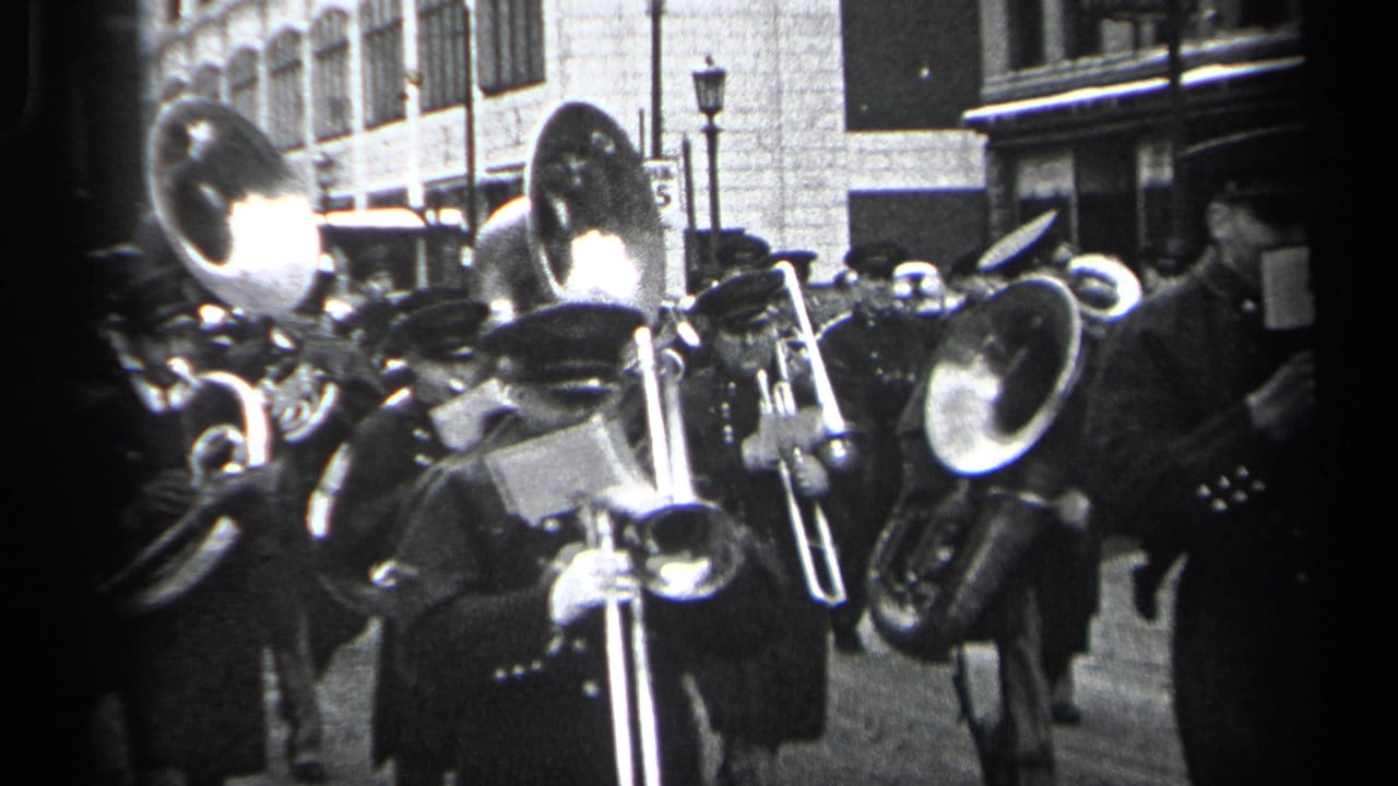 Uniformed marching band members play brass instruments on a city street.
