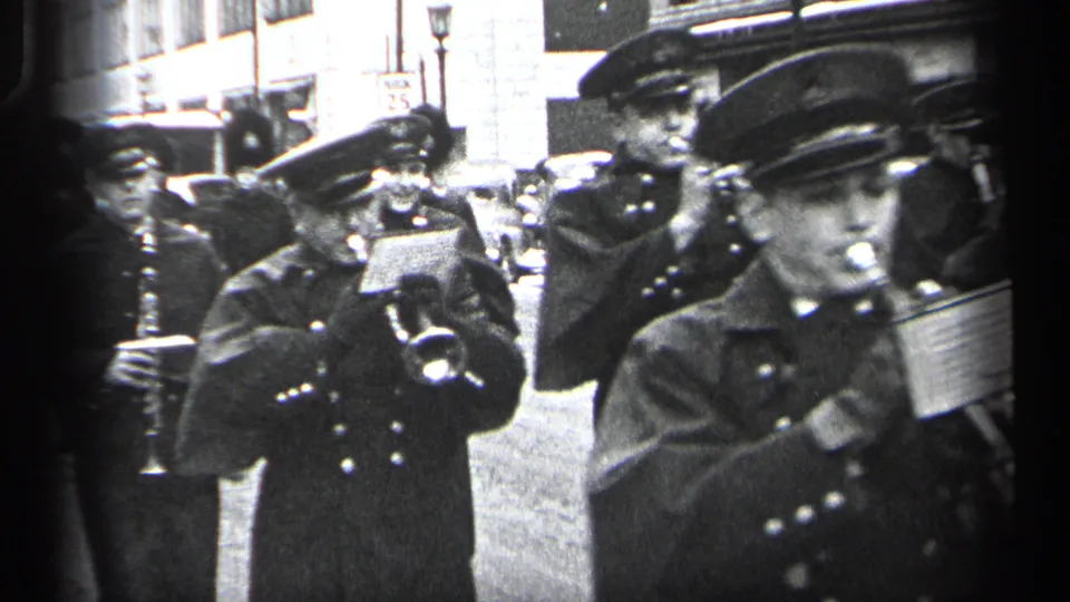Uniformed band members in a 1937 Cleveland parade move through the frame with brass instruments, sheet music cards, and drum hardware visible.