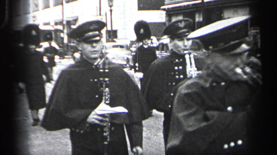 Cleveland parade frame from the supplied 1937 clip showing uniformed adults marching with drum and trumpet in a downtown street setting.
