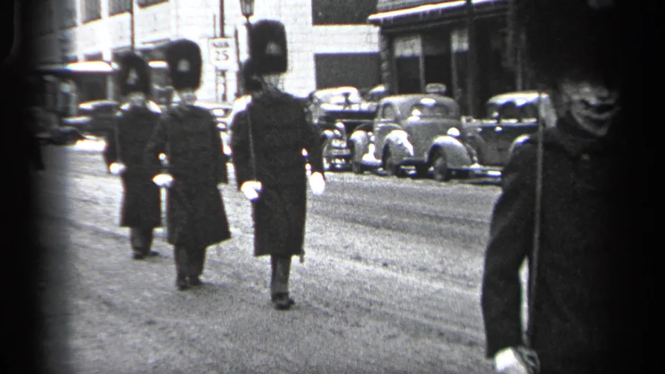 Two guards continue down the Cleveland street while a closer uniformed marcher crosses the right edge of the frame.