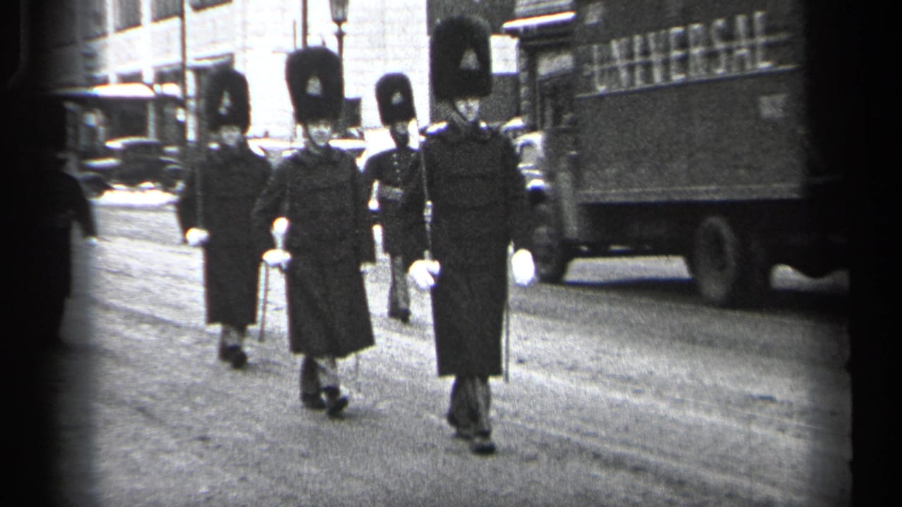 Uniformed guards march down a city street beside vintage vehicles and storefronts.