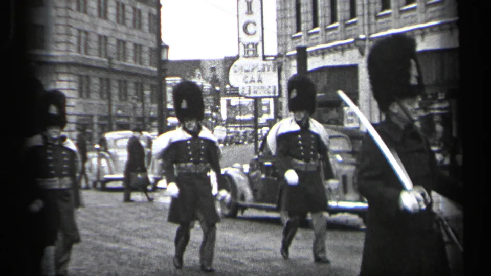 Uniformed guards with bearskin-style hats and white gloves march past automobiles and commercial buildings in Cleveland.