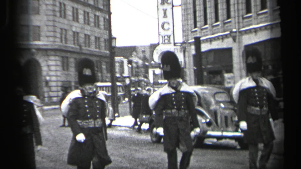 Two ceremonial guards march near the camera on a Cleveland street, with 1930s automobiles and building facades behind them.