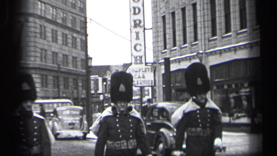 A guard passes close to the lens while other uniformed guards and 1930s automobiles remain visible on the Cleveland street.