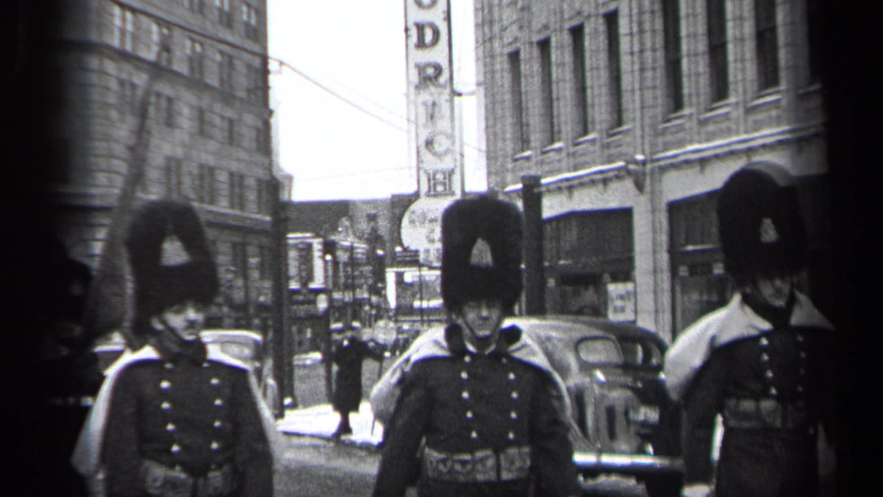 1937 Cleveland street parade with uniformed marchers in tall fur hats passing storefronts, parked cars, and a vertical sign.