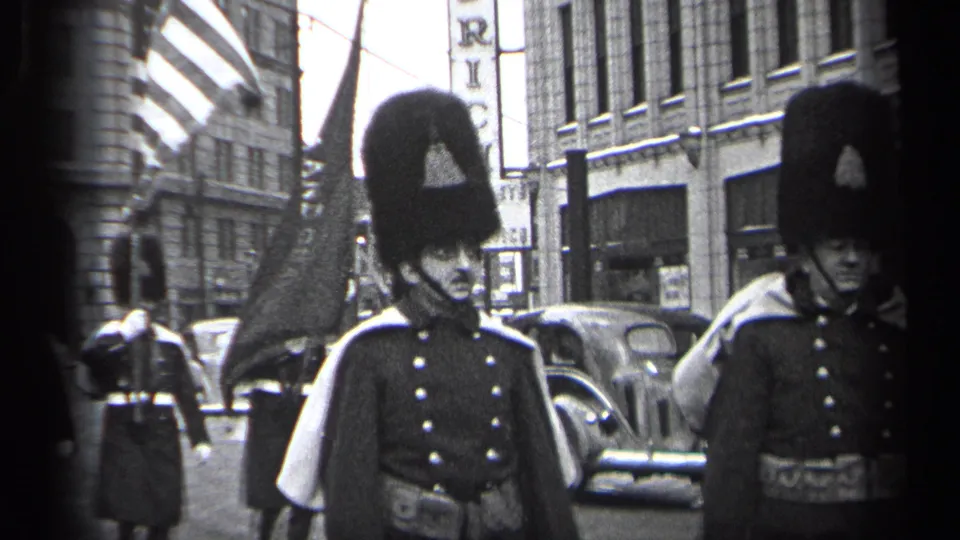 Uniformed parade participants in 1937 Cleveland pass near the camera with parked cars and commercial buildings behind them.