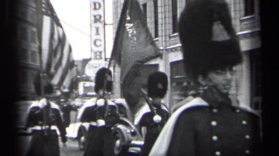 1937 Cleveland parade view with flag bearers, uniformed marchers, tall hats, and parked period automobiles along the curb.