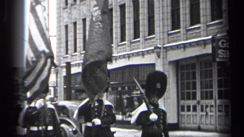 Ceremonial marchers in 1937 Cleveland carry flags and rifles past storefront windows, parked cars, and vertical business signage.
