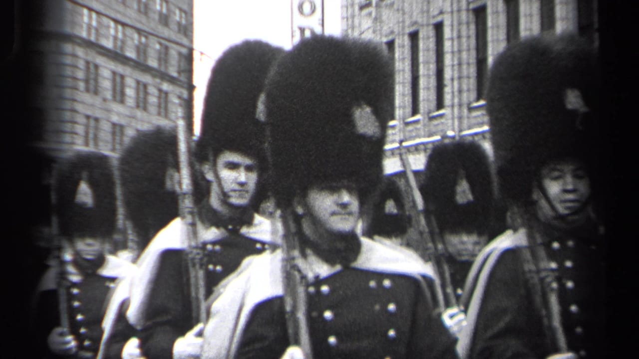 Uniformed men in tall dark hats march with rifles on a city street.