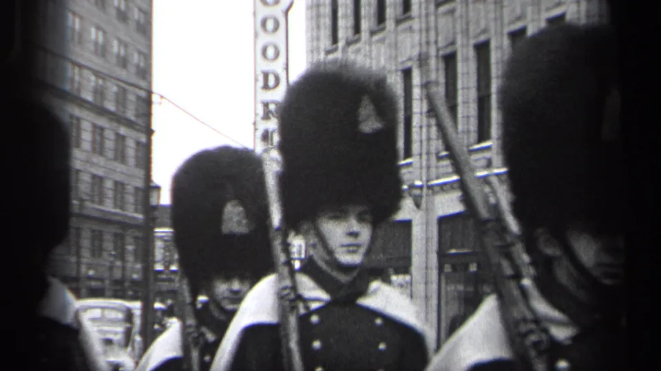 Close street-level frame of Cleveland parade marchers in tall bearskin-style hats with rifles and city signage behind them.