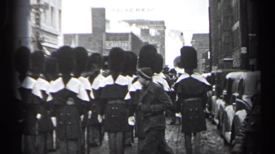 1937 Cleveland parade view of uniformed marchers in tall dark hats and white collars moving away from the camera on a city street.