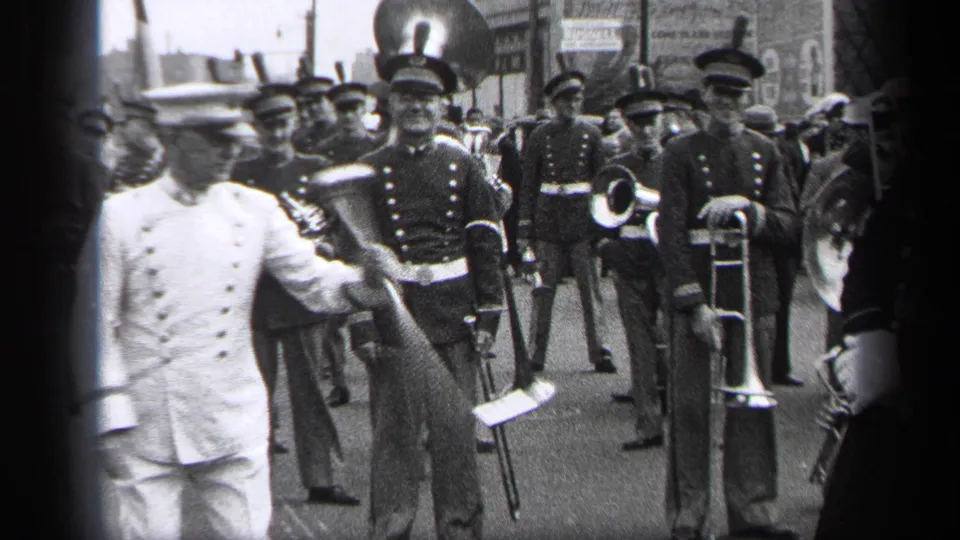 A white-uniformed parade leader precedes brass band musicians with trombones and a tuba on a Cleveland city street in 1937.