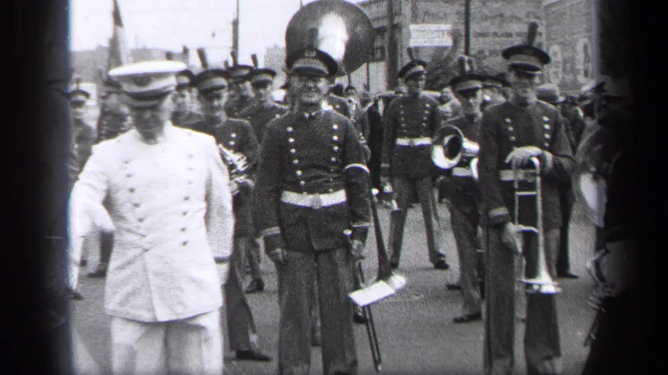1937 Cleveland parade footage showing a white-uniformed baton leader in front of dark-uniformed marching band musicians.