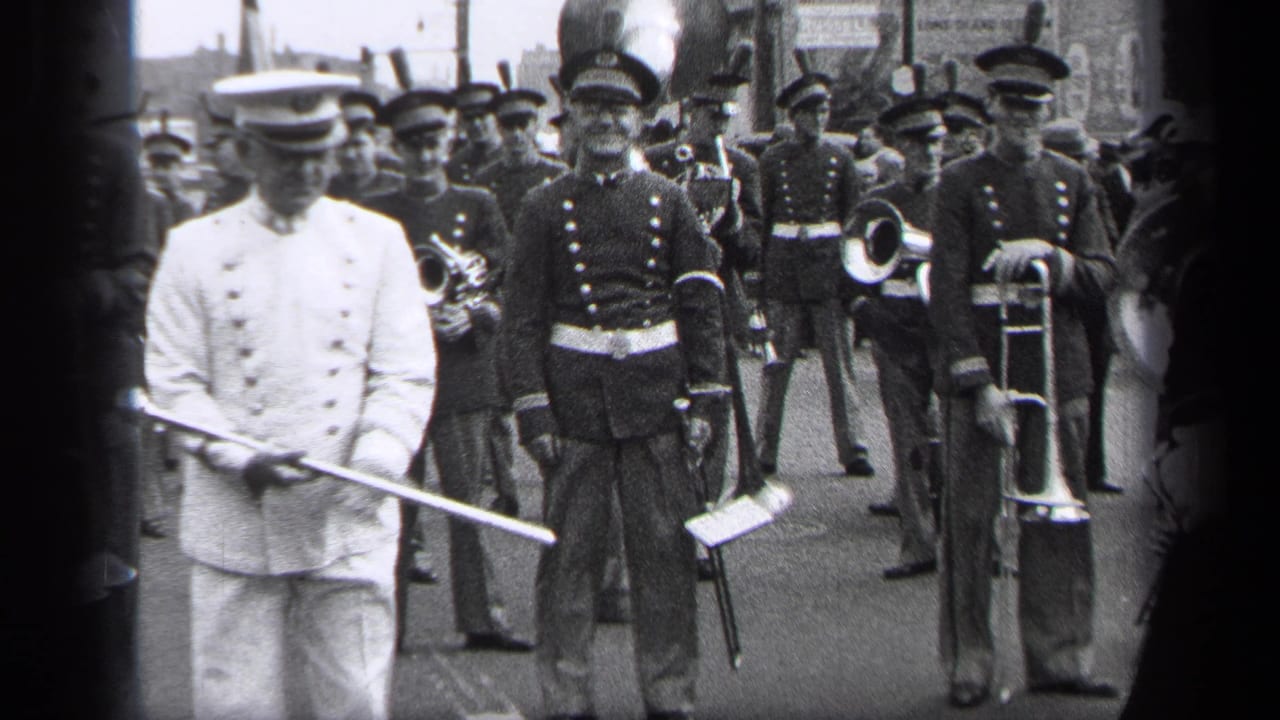 White-uniformed parade leader holds a baton while band members line up behind him.