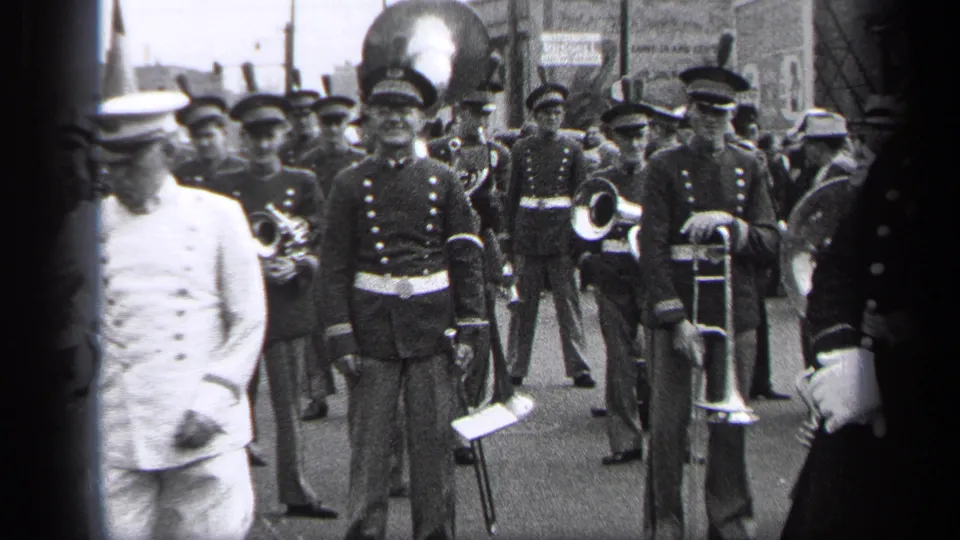 The 1937 Cleveland street parade continues with the baton leader moving past the camera and musicians visible behind him.