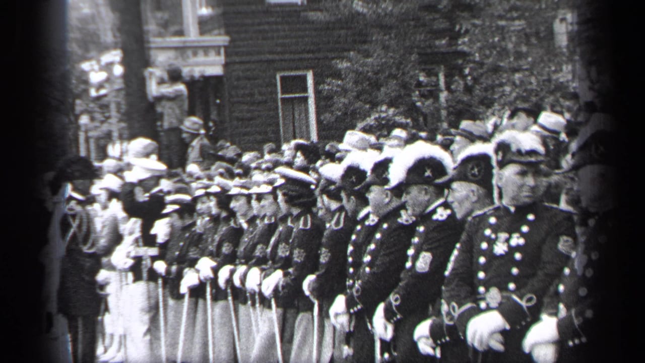 Uniformed marching band members stand in formation along a crowded city street.