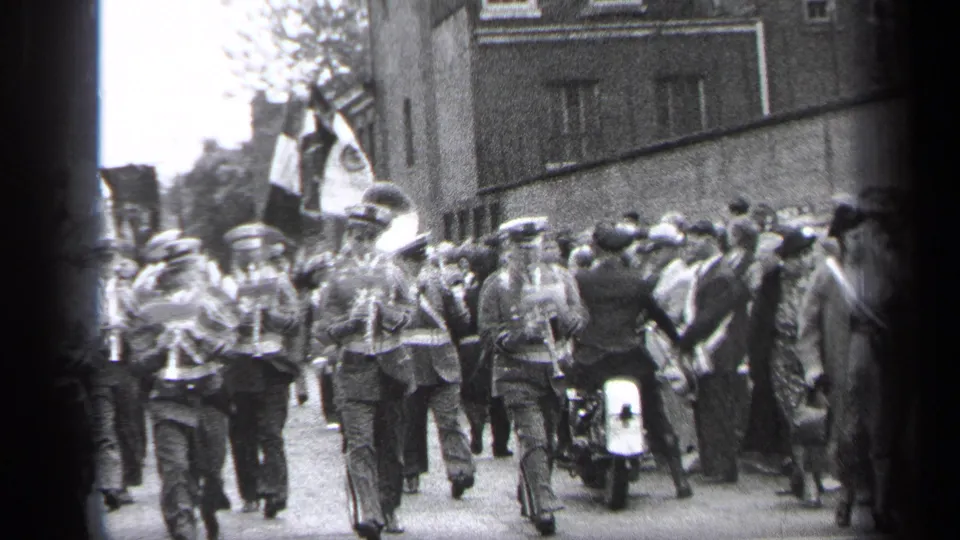 A marching band passes along a Cleveland street in 1937 as spectators cluster near buildings and a motorcycle escort appears in the route.