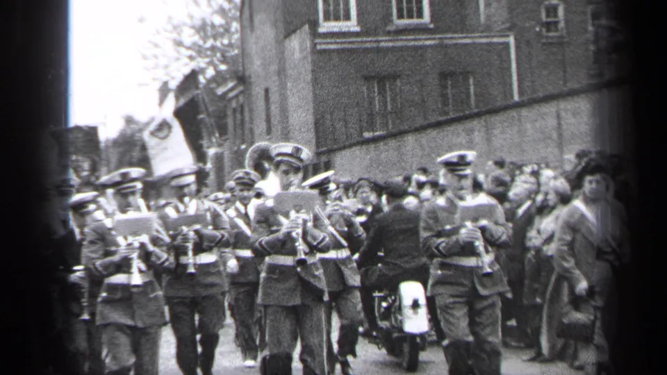 Uniformed musicians with instruments march through a 1937 Cleveland street parade as spectators watch beside brick buildings.