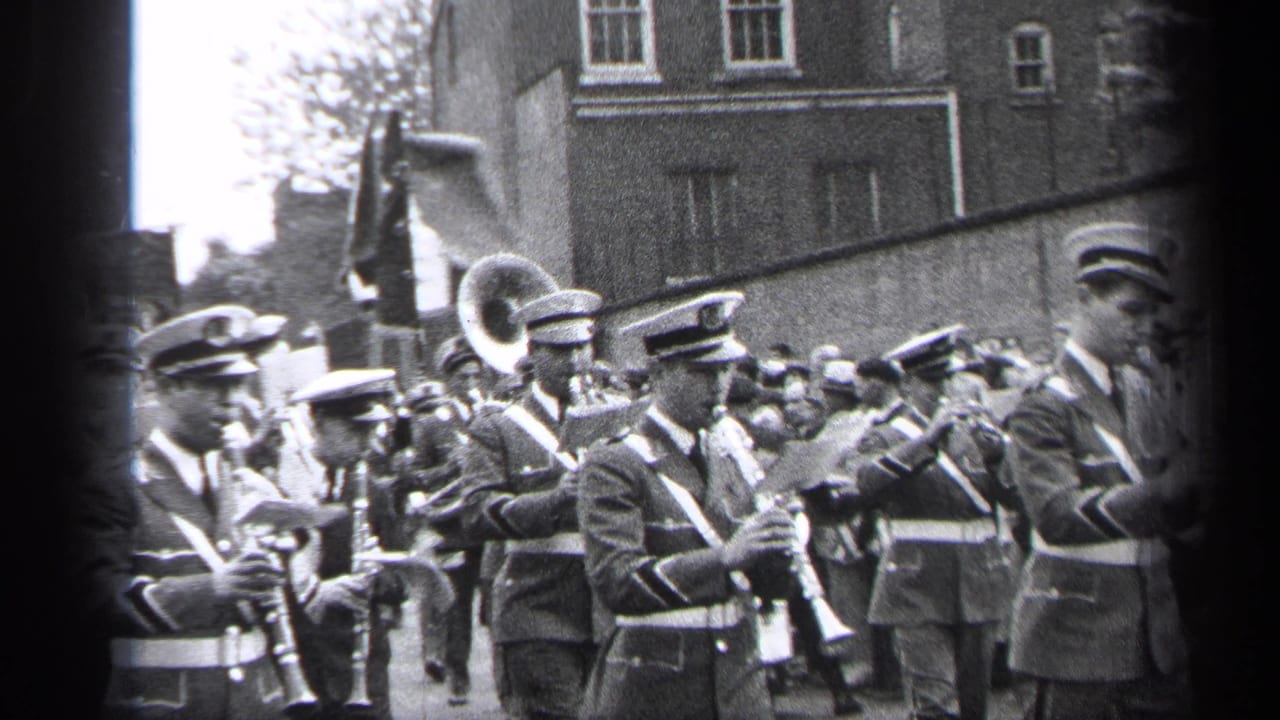 Band musicians in caps play instruments while marching past a crowd.