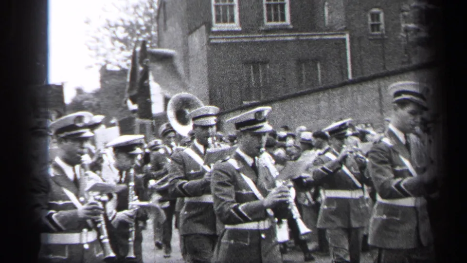 Uniformed musicians in 1937 Cleveland carry clarinets, brass instruments, and a large tuba or sousaphone bell during a parade.