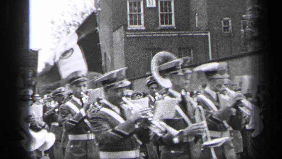 At the end of the 1937 Cleveland parade clip, uniformed musicians carry sheet music and brass instruments while spectators line the street.