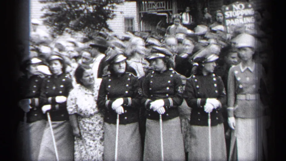 Uniformed women in Cleveland stand shoulder to shoulder with canes while spectators crowd behind them near a no-stopping parking sign.