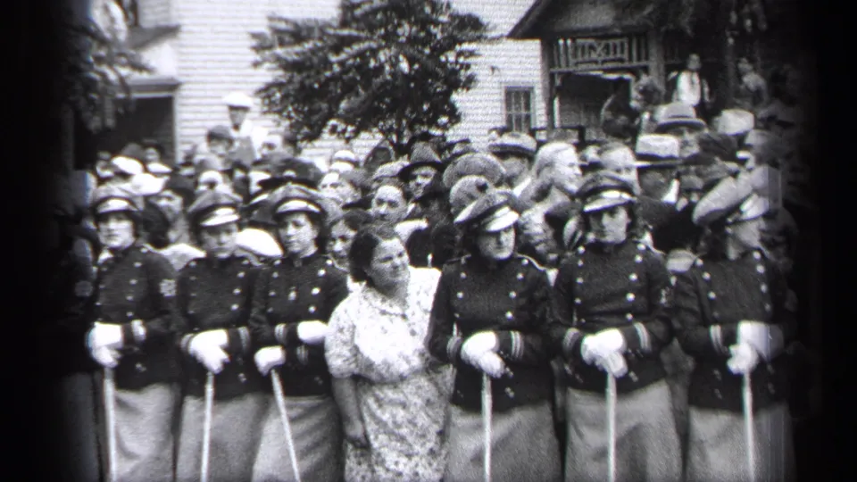A Cleveland street gathering shows uniformed women with canes standing in a row as a crowd in period clothing watches behind them.