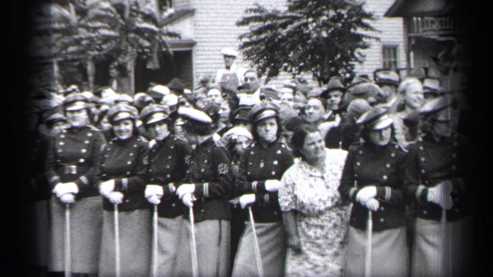 Women in dark uniforms and caps hold canes during a 1937 Cleveland public gathering, with a patterned-dress spectator visible in front.