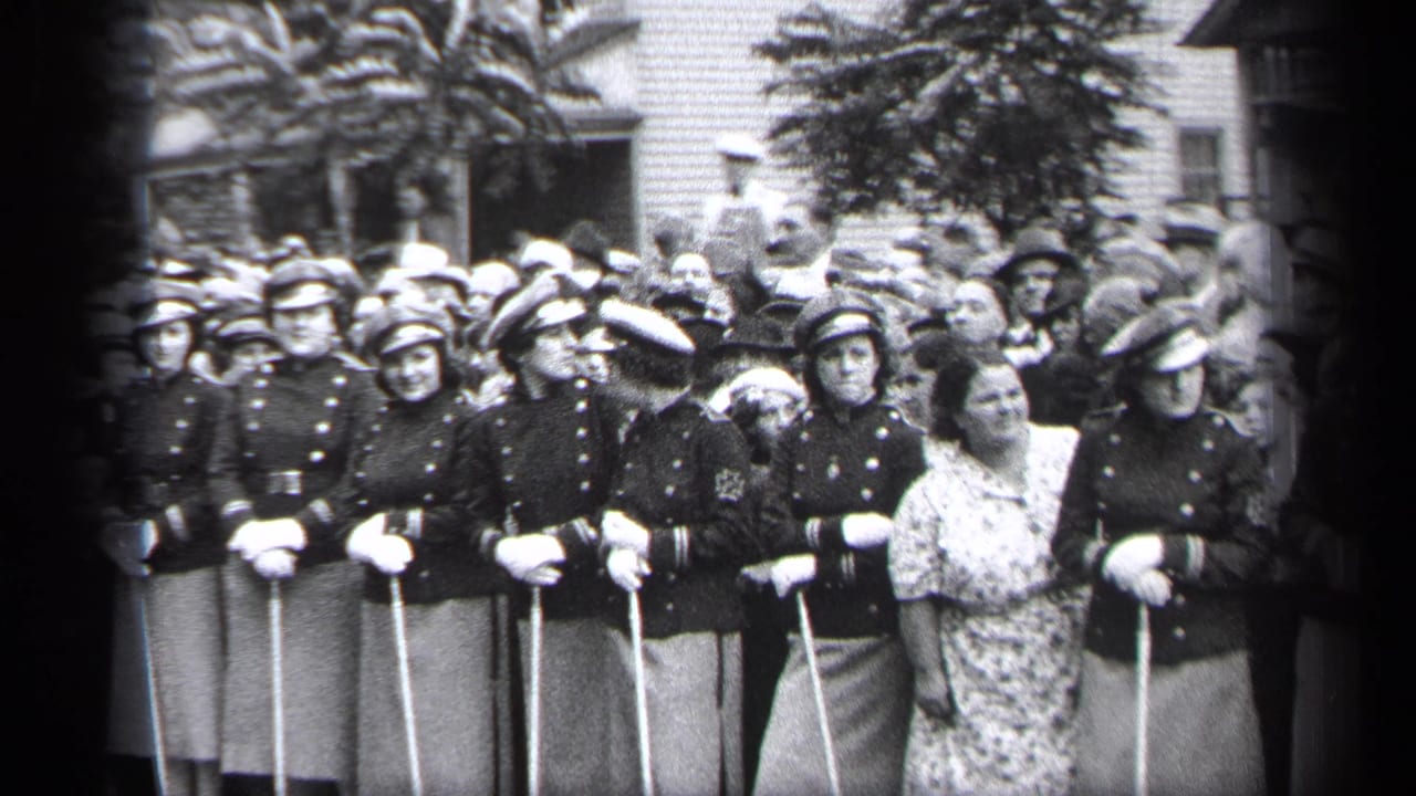 In Cleveland in 1937, uniformed young women with caps and white gloves stand in formation with long poles while a crowd watches.