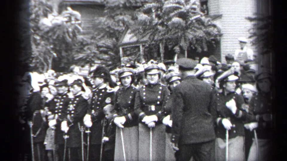 A man appears to address or pass the uniformed formation of young women holding poles at an outdoor Cleveland gathering in 1937.