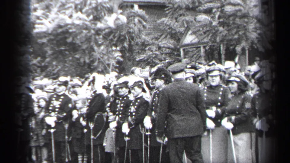 The final frame shows the capped man near the front row of the 1937 Cleveland formation, with uniformed young women and a crowd behind him.