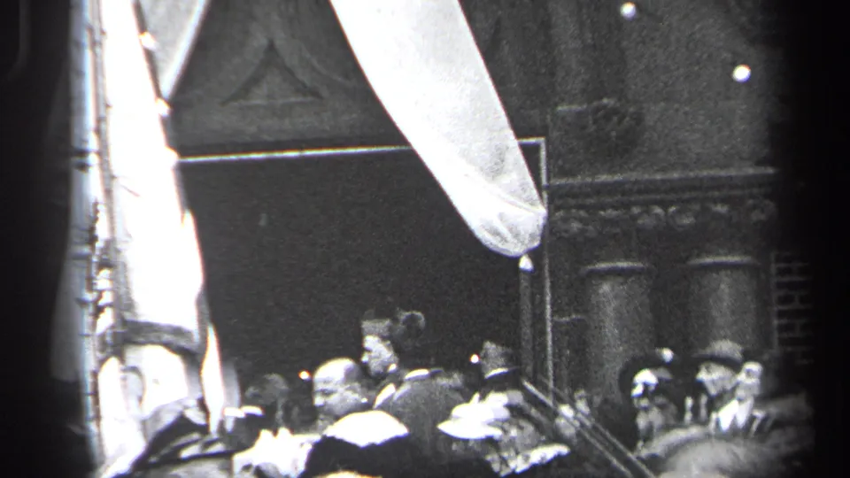 1937 Cleveland home-movie frame showing a dense public crowd, a large vertical flag, and draped fabric near a building entrance.