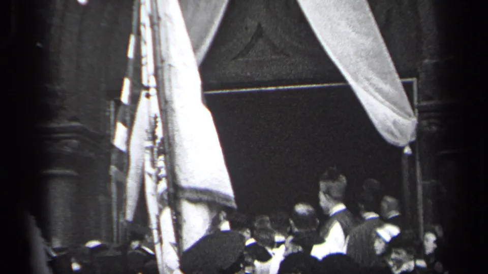 1937 Cleveland frame with men in suits and hats gathered beside a tall flag and fabric drape at a public event.