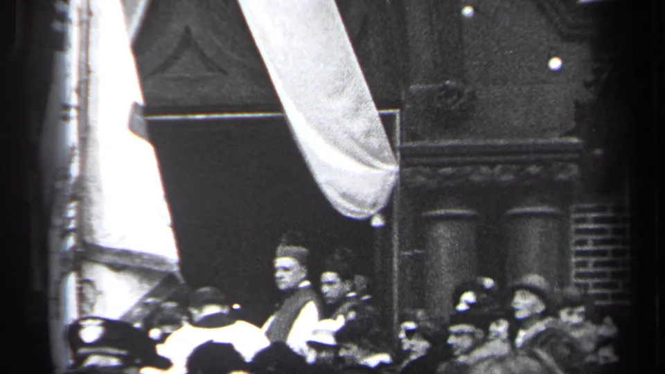 1937 Cleveland home-movie frame showing spectators in hats near a street parade, with a large light banner or fabric shape overhead.