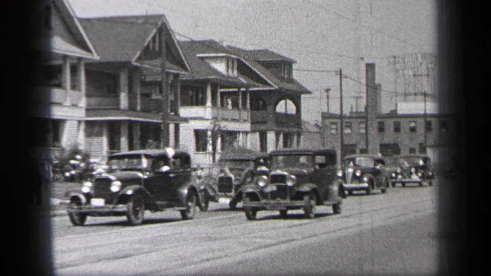 1937 Cleveland parade frame showing several 1930s automobiles driving past houses, utility poles, and curbside onlookers.