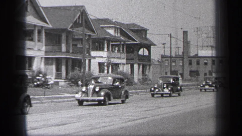 A 1937 Cleveland street scene shows vintage cars moving past houses, with a small motorcycle-like vehicle near the left curb.