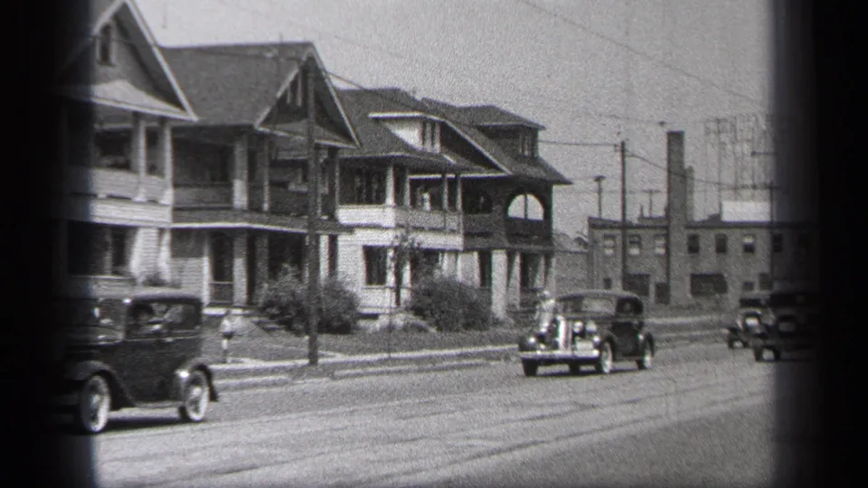 1937 Cleveland street view with late-1930s cars moving past two-story houses, utility poles, and overhead wires.