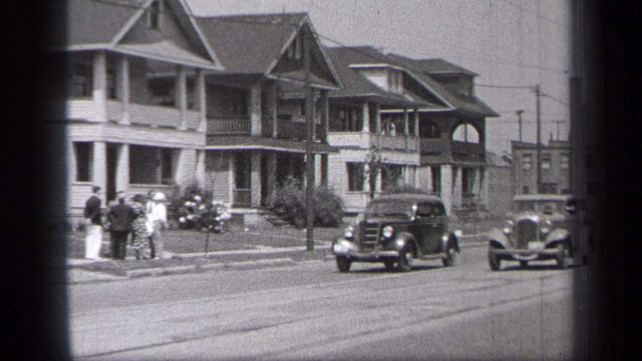 Small group stands on the sidewalk as cars travel along the street.