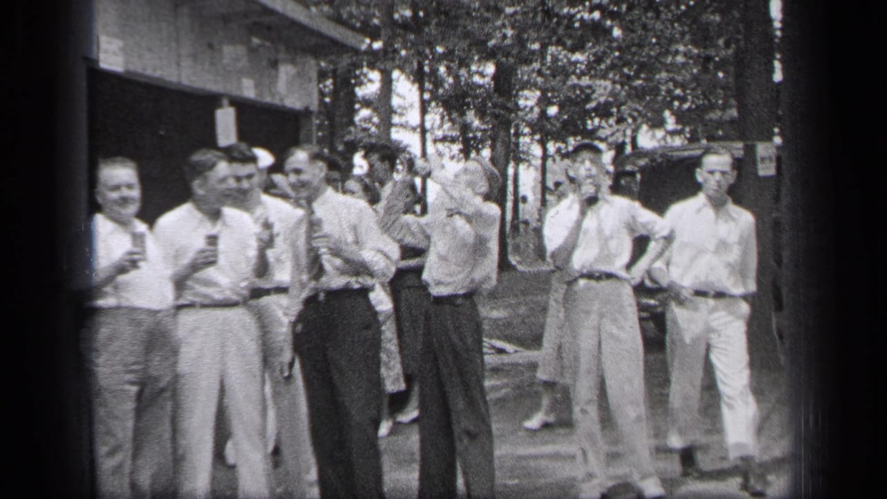 Men stand outdoors with drinks near a building and trees.