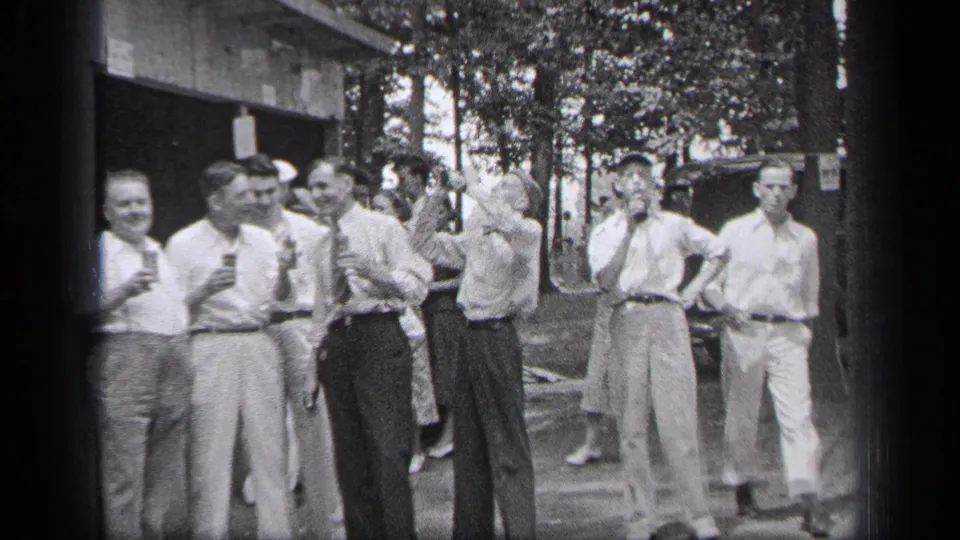 Adult men in 1937 Cleveland stand outside with cups or glasses near a building, trees, and a parked car.