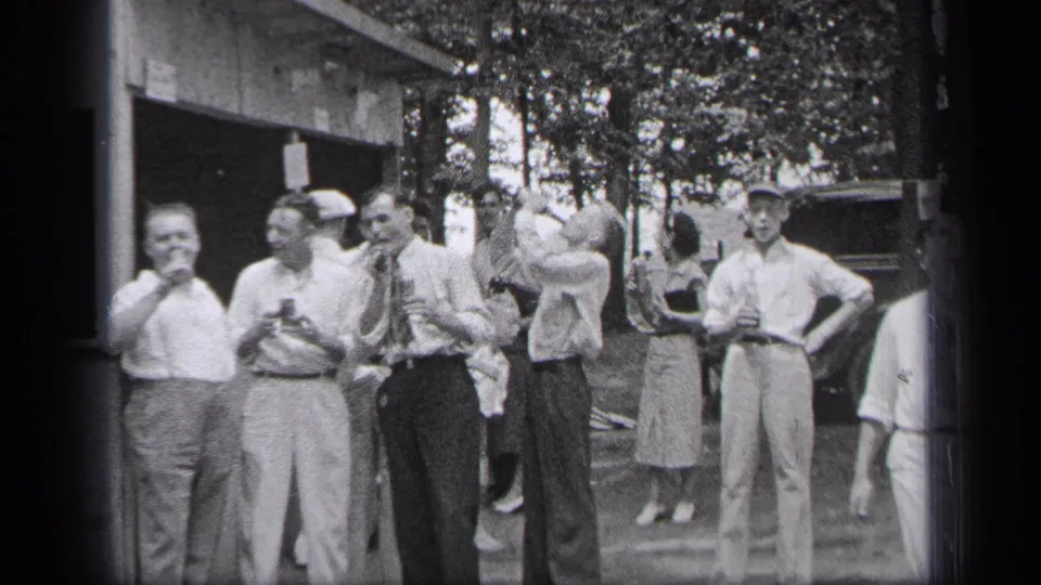 A group of adult men in Cleveland, Ohio, smile outdoors as one man raises a drink during a 1937 home-movie moment.