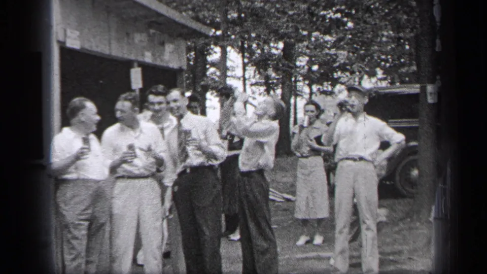 Adults in 1937 Cleveland gather outside a building, with one man drinking and others facing the camera near a parked car.