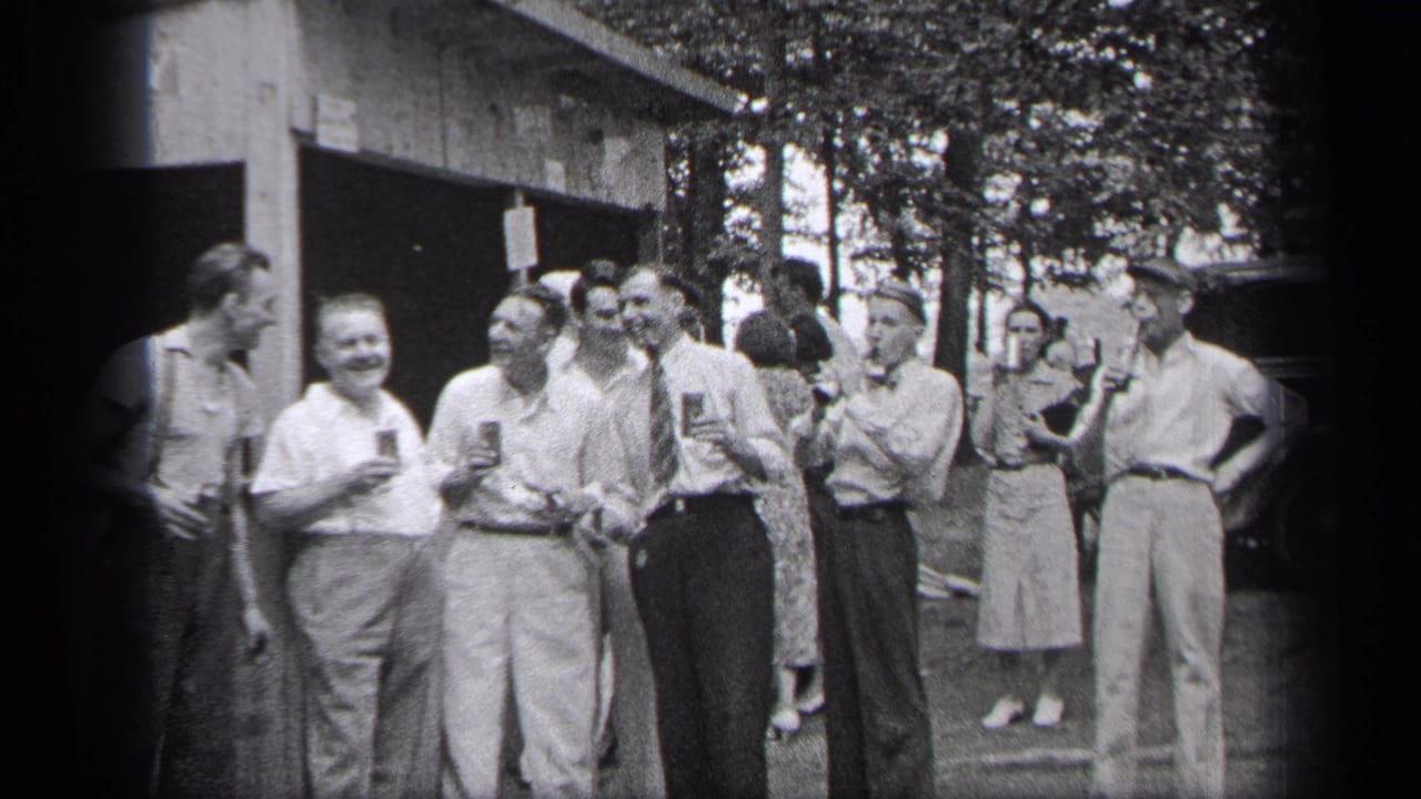 Adults stand outdoors with drinks near a rustic building and trees.