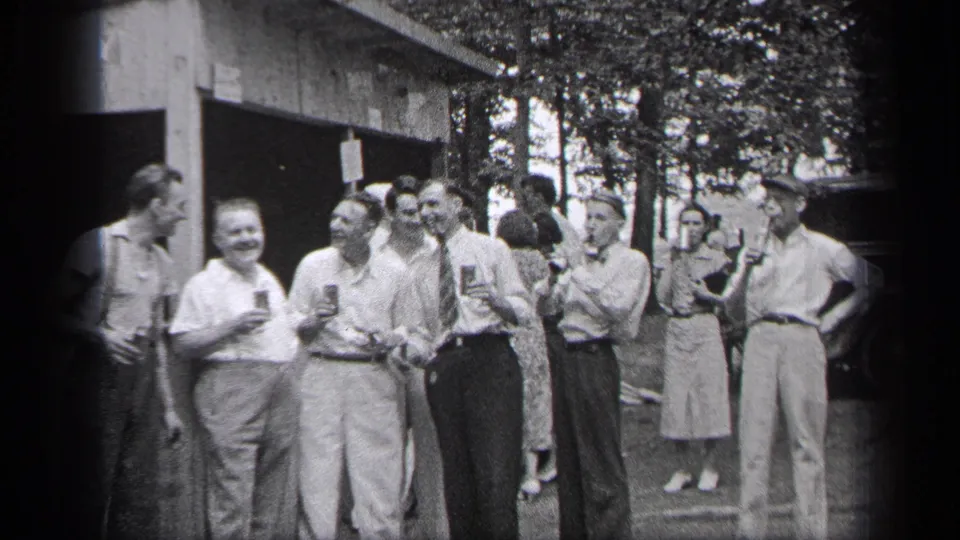 1937 Cleveland home-movie frame of adults in shirts, ties and dresses talking with drinks outside a building.