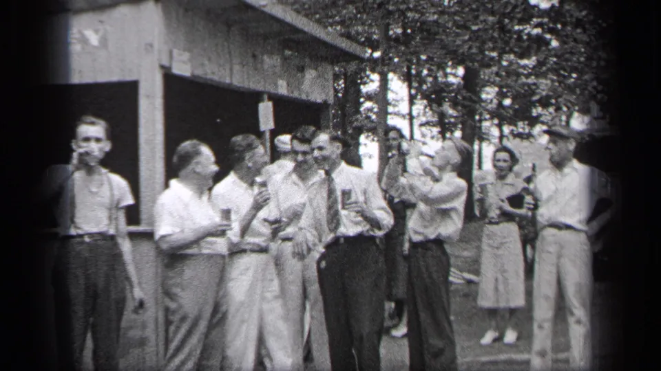 Adults in 1930s attire gather outside in Cleveland, with men holding drinks and women standing nearby.