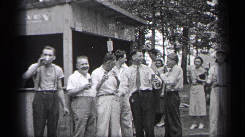 Adults in late-1930s clothing smile, turn and converse with drinks outside a Cleveland building.