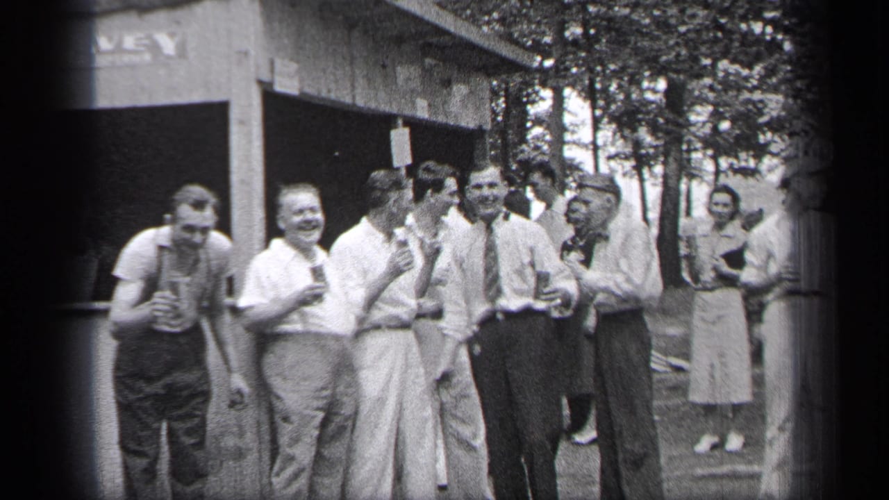 Men in 1930s clothing laugh and hold drinks outside a small wooden stand.
